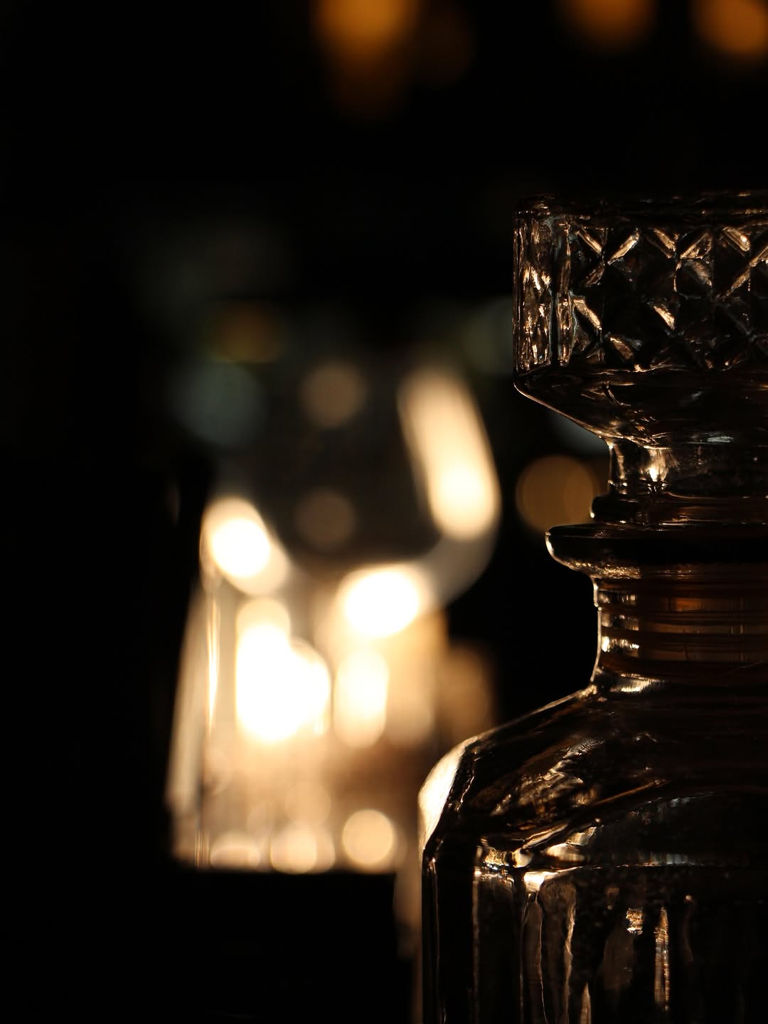 A crystal decanter glowing against golden bokeh candlelight at the Maia bar