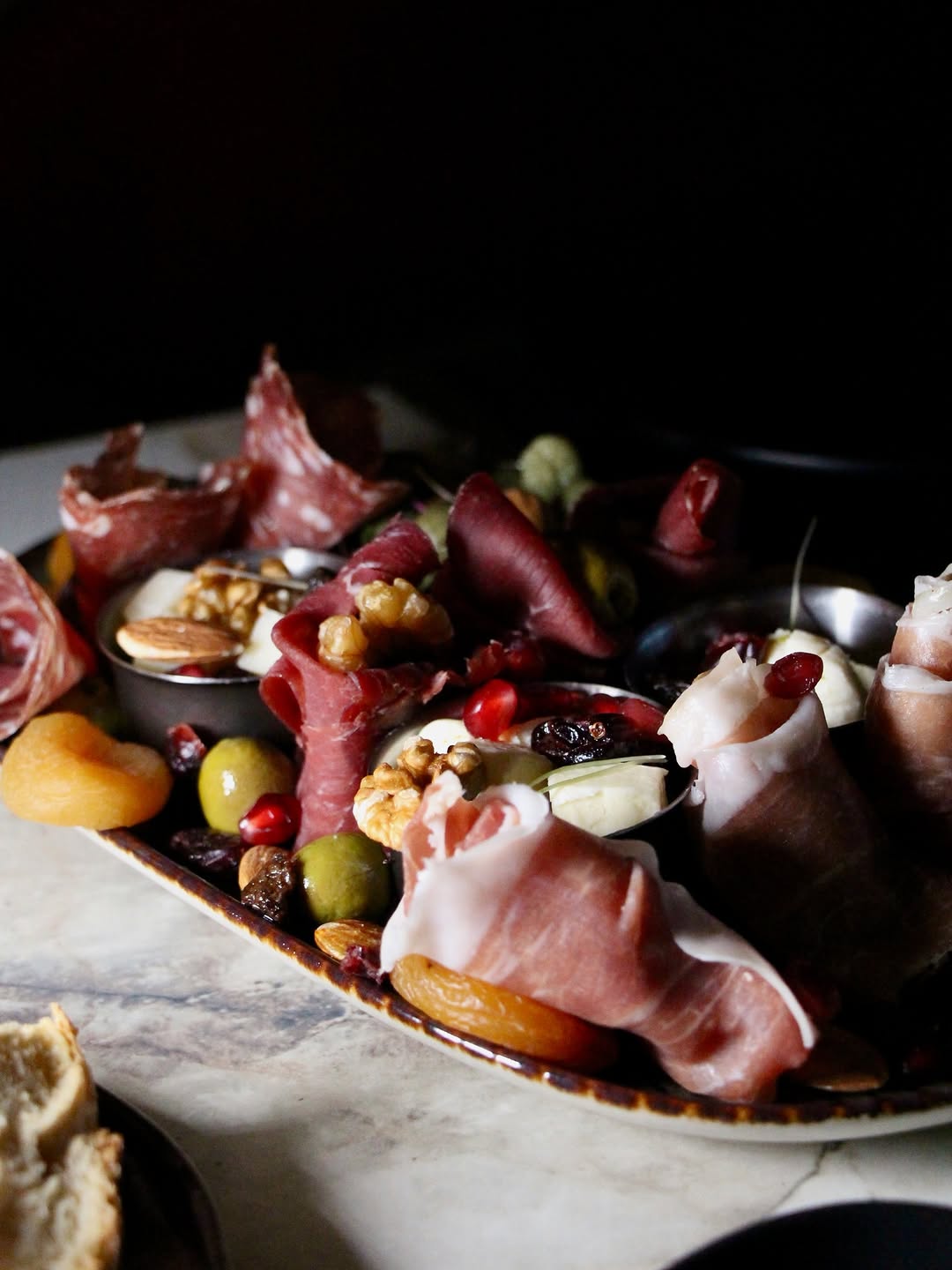 An abundant charcuterie board of cured meats, green olives, pomegranate, walnuts and apricots on marble