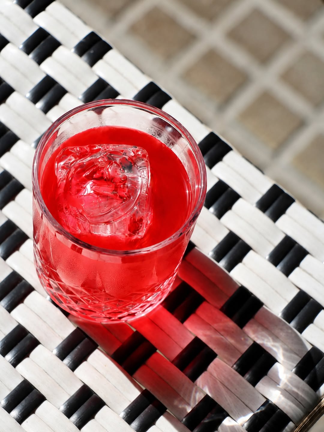 An overhead shot of a scarlet cocktail in a crystal glass on black-and-white wicker furniture