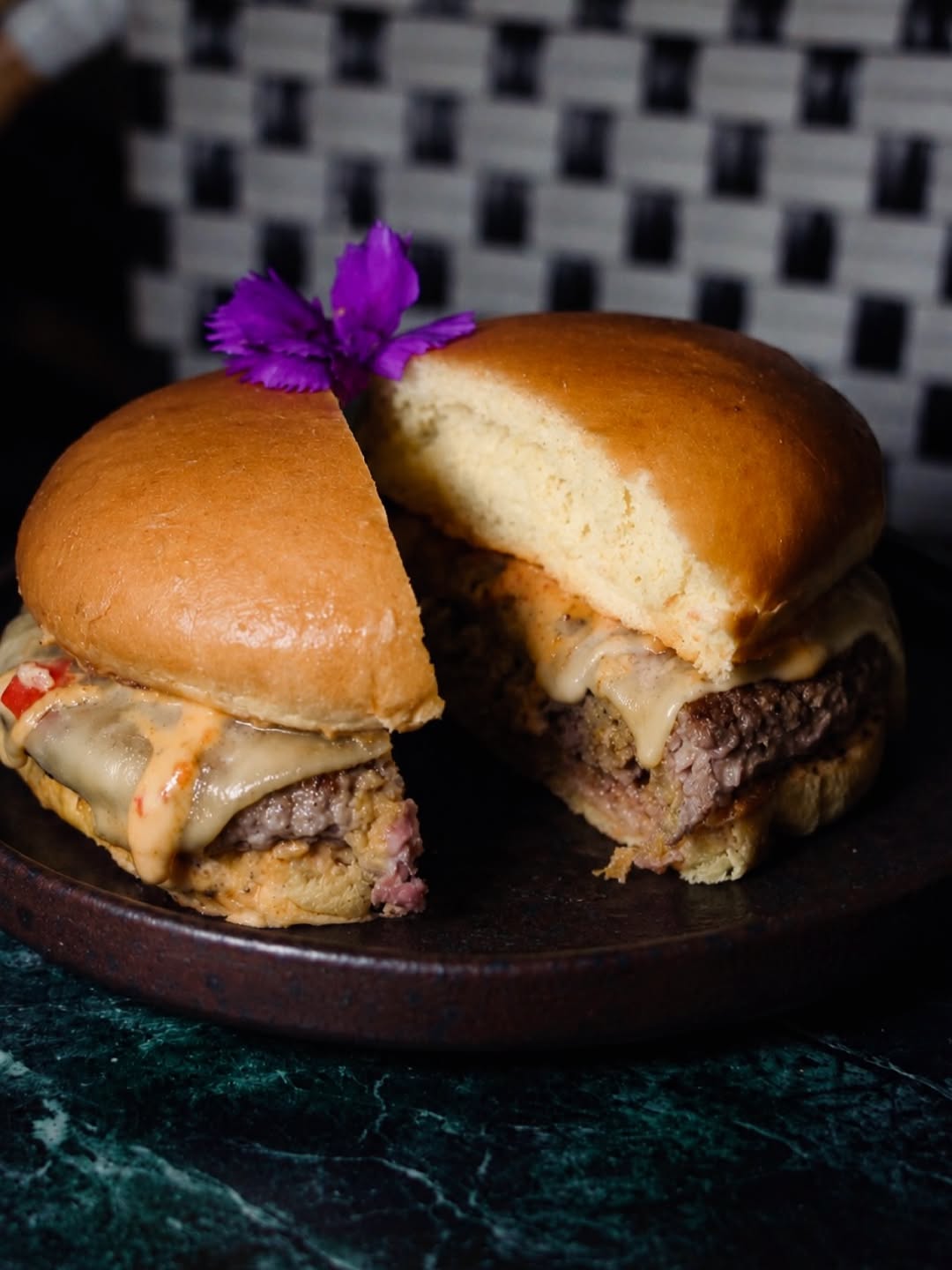 Japanese Wagyu burger sliced in half on a dark ceramic plate with a purple flower garnish at Maia Beirut
